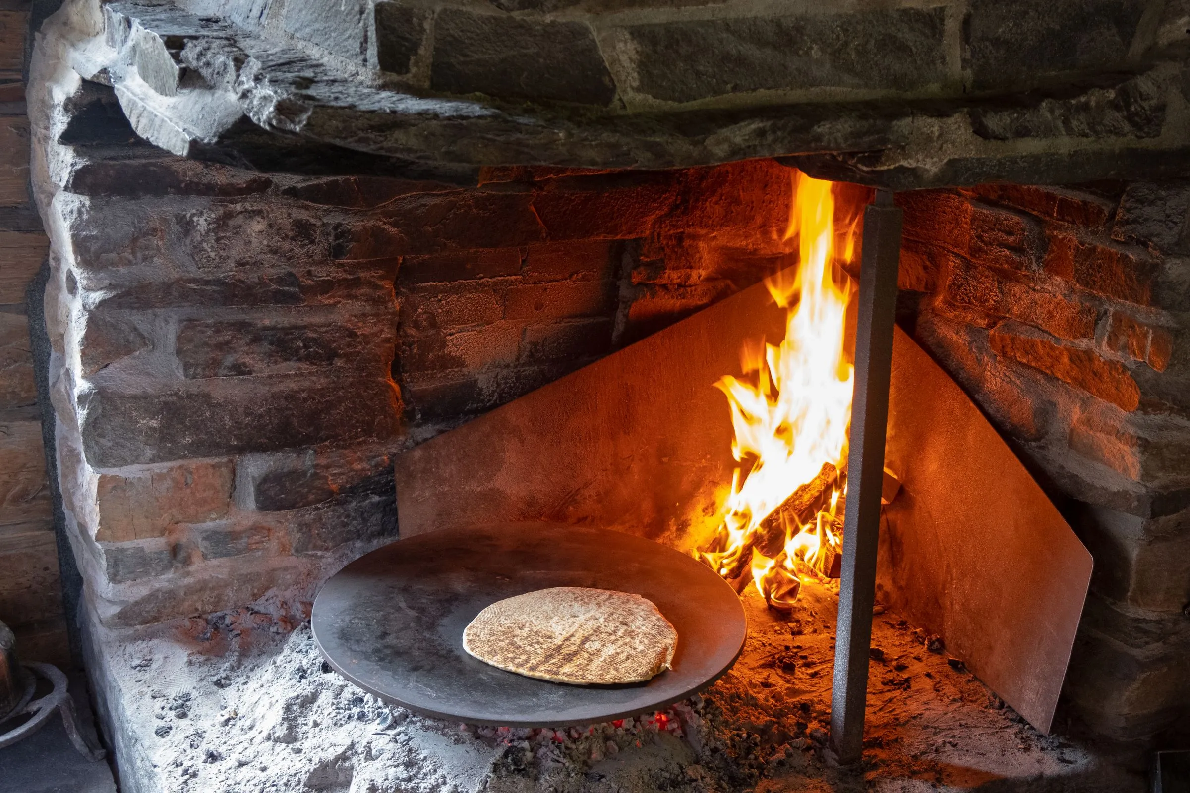 Fladenbrot auf einer Eisenplatte vor offenem Holzfeuer in einem gemauerten Ofen